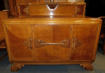 An early 20thC oak dining suite, comprising a sideboard, carved with flowers and scrolling leaves, having a central door opening to reveal four drawers, flanked by a pair of cupboard doors, enclosing shelves, to the right with a four recess bottle holder, - 2