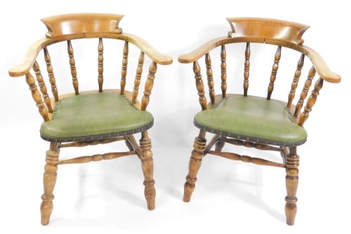 A pair of Victorian oak smoker's bow chairs, with later green button leatherette seats, raised on turned legs.