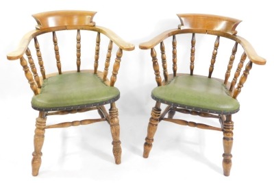 A pair of Victorian oak smoker's bow chairs, with later green button leatherette seats, raised on turned legs.