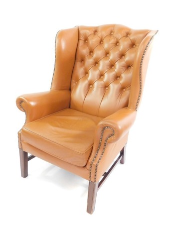 A Georgian style mahogany wing armchair, upholstered in button back tan leather, with loose cushion seat, raised on tapering square legs.