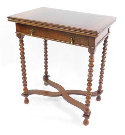 A Carolean style oak fold over card table, with a single frieze drawer, having brass pear drop handles, on bobbin turned supports, united by an X frame stretcher, 71cm high, 61cm wide, 40cm deep.
