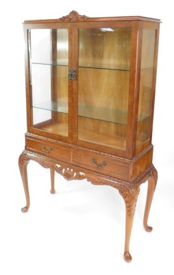 A Chechik Limited mid century burr walnut display cabinet, the foliate carved top above a pair of doors, enclosing two glass shelves, above a pair of frieze drawers, over leaf carved cabriole legs, 158cm high, 90cm wide, 37.5cm deep,
