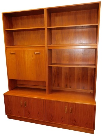 A G-Plan 1960's teak lounge unit, the two section top with an arrangement of five shelves and a drop down drinks cabinet, above a sideboard base with four doors, raised on a plinth base, 198cm high, 162.5cm wide, 46cm deep.