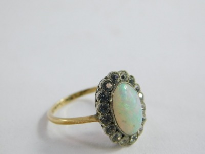 A 9ct gold opal dress ring, the central oval opal in platinum rub over setting, surrounded by tiny white stones, on a raised basket setting, on yellow gold band marked 9ct and sil,  size M, 2.5g all in, boxed.  - 3