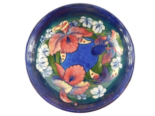 A Moorcroft pottery bowl decorated in the Frilled and Slipper Orchid pattern, against a blue ground, painted and impressed marks, 22cm diameter. (AF)