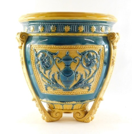 A Wedgwood late 19thC blue and yellow pottery jardiniere, moulded with panels of classical vases, flowers and foliate scrolls, raised on three leaf moulded scroll feet, impressed and painted marks, 34cm high, 32cm wide. (AF)