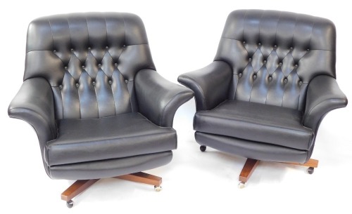 A pair of G-Plan mid century black vinyl swivel chairs, each on a wooden base with castors, with button back and detailing, 85cm high, 92cm wide, 85cm deep.