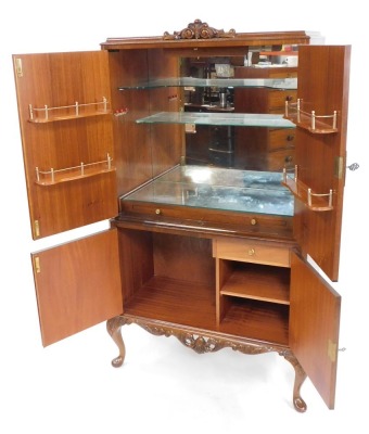 A mid century burr walnut cocktail cabinet, the foliate carved top over a pair of doors, opening to reveal a mirror back, glass shelves and fitted interior, above a further door enclosing a drawer and shelves, on cabriole legs, 159cm high, 85cm wide, 41cm