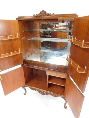 A mid century burr walnut cocktail cabinet, the foliate carved top over a pair of doors, opening to reveal a mirror back, glass shelves and fitted interior, above a further door enclosing a drawer and shelves, on cabriole legs, 159cm high, 85cm wide, 41cm - 2