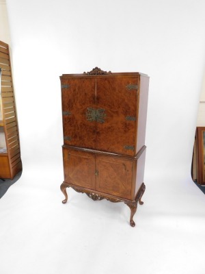 A mid century burr walnut cocktail cabinet, the foliate carved top over a pair of doors, opening to reveal a mirror back, glass shelves and fitted interior, above a further door enclosing a drawer and shelves, on cabriole legs, 159cm high, 85cm wide, 41cm - 3