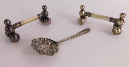 A group of silver and silver plated cutlery, comprising a pair of mother of pearl and silver plated knife rests, together with a silver plated caddy spoon, with floral pierced detailing. (3)