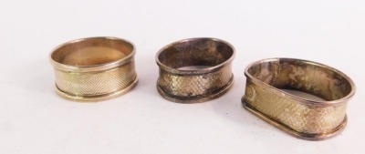 Three silver napkin rings, to include an oval engine turned decorated napkin ring with vacant shield panel, circular napkin ring and a hammered napkin ring, all Birmingham, 1¼oz. (2, boxed)