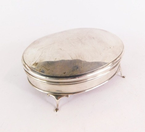 A George V silver dressing table box and cover, of oval form, monogram engraved, with a red velvet lined interior, base on four outsplayed legs, Birmingham 1918, 5¼oz.