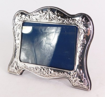 A silver neo-classical style photograph frame, the arched top with embossed detailing of cherubs and vines with fruits, on a blue velvet lining, maker's stamp WW Sheffield 1992, picture size 9cm x 12cm, frame size 15cm x 17cm.