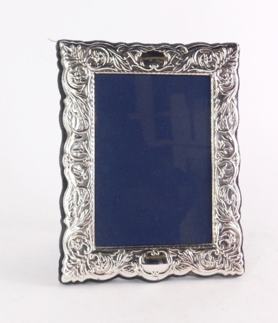 A silver photograph frame, the rectangular frame with floral and leaf scroll detailing with a vacant shield top and bottom, on a blue velvet lining, maker's stamp RC, Sheffield 1996, picture size 10.5cm x 8cm, frame size 17cm x 13cm.