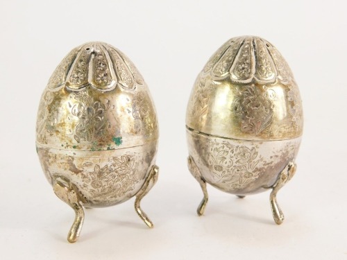 A pair of Eastern salt and pepper shakers, of ovoid form with engraved floral detailing, on three scroll feet, white metal, unmarked, 3½oz.