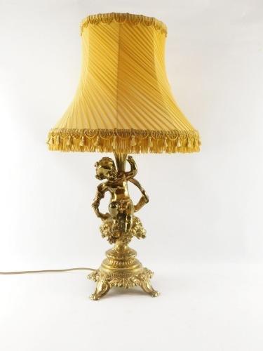 A continental brass cherub table lamp, the stem with putto holding a flower, on a floral seated base, with four out splayed legs, with orange shade, 64cm high.