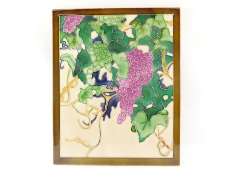 A painted art pottery panel, rectangular, depicting grapes and vines, on material backing, 41cm x 33cm.