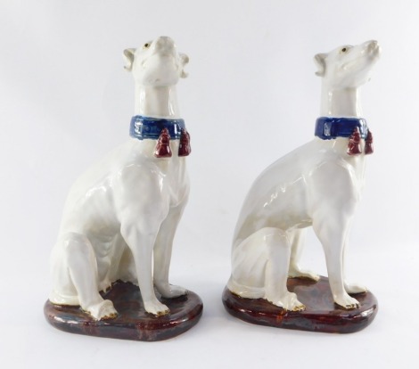 A pair of late 19thC style pottery greyhound figures, in seated pose, with a blue collar, on a brown coloured base, 35cm high.
