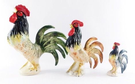 Three Babbacombe Pottery cockerel figures, by Lownds Pateman, each modelled standing 30cm high, 24cm high and 15cm high.