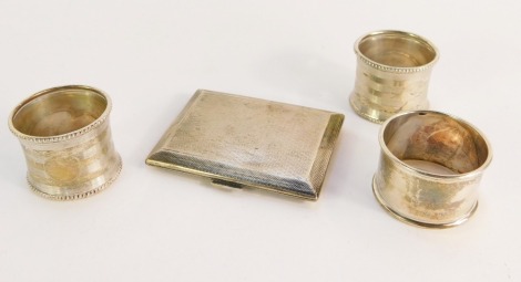 A group of silverware, comprising three silver napkin rings, two engine turned, one of plain design, together with a silver cigarette case, bearing internal initial V, with outer engine turned decoration, London 1931, 4½oz. (4)