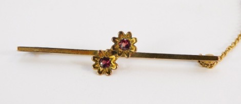 A 9ct gold bar brooch, with applied two flower detailing set with garnets, with single pin with safety chain, 3.9g all in, 5.5cm wide.