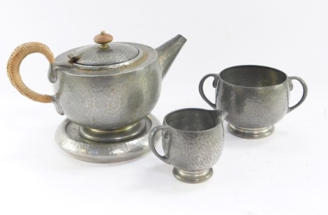 A Liberty Tudric pewter four piece tea set, comprising teapot and stand, milk jug and sugar bowl, each with hammered finish, with a woven detailed handle, no 01216, impressed marks..