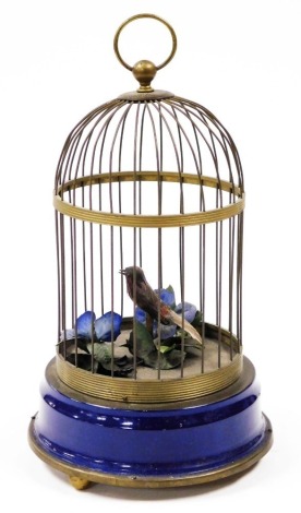 A 20thC brass and tin plate musical automaton bird cage, containing a feather clad bird and various artificial flowers, with a blue painted base, 33cm high including handle.