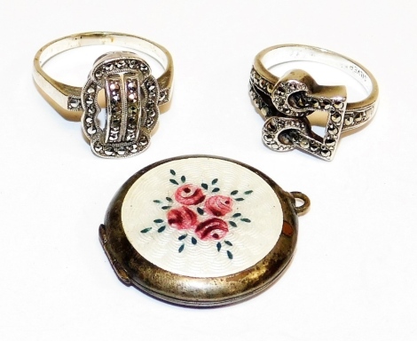 A group of silver jewellery, to include two silver and marcasite bow dress rings, and a silver and enamel set locket, with white enamel backing and four rose painted details.