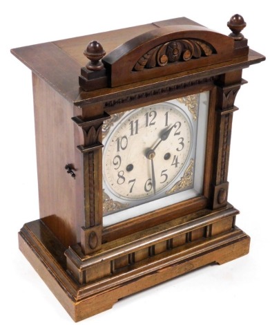 An early 20thC walnut cased mantel clock, with a silvered square dial, brass spandrels, silvered chapter ring bearing Arabic numerals, eight day movement with coil strike, the case of architectural form, no key, the case 33cm high.