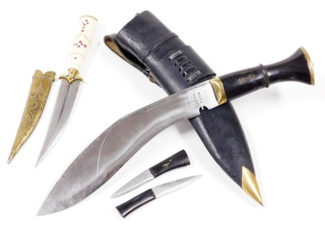 A late 20thC Nepalese kukri, the blade dated 1994 with composition handle and brass pommel, the leather scabbard containing two further small daggers, 43cm long, and a small eastern dagger with engraved brass scabbard and bone handle. (2)