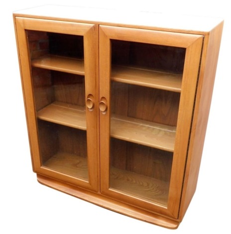 An Ercol light elm bookcase, with a pair of glazed doors enclosing two shelves, raised on a plinth base, 100cm high, 92cm wide, 29cm deep.