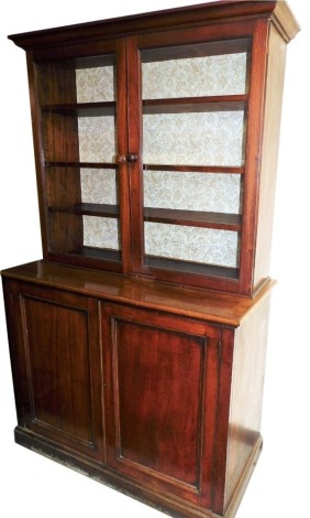 A Victorian mahogany cupboard bookcase, the out swept pediment above two glazed doors with wooden handles enclosing three shelves, above a pair of cupboard doors, raised on a plinth base, 206cm high, 128cm wide, 57cm deep.