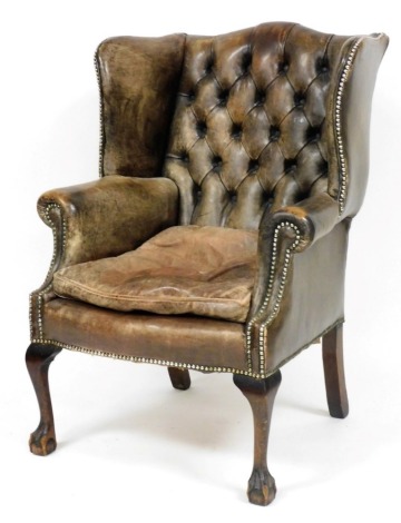 An early 20thC tan leather wing back armchair, with button back and stud detailing to top, on oak cabriole legs terminating in ball and claw feet, 105cm high.