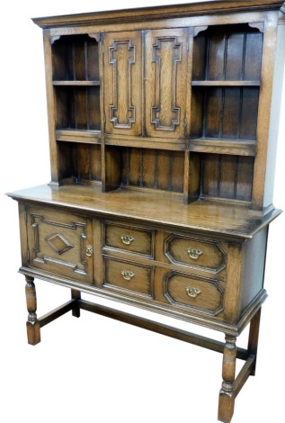 An early 20thC oak dresser, the out swept pediment over two panelled doors and an arrangement of shelves, the base with two drawers beside a cupboard door, raised on turned legs united by an H framed stretcher, 183cm high, 137cm wide, 49cm deep.