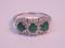 A triple cluster dress ring of three emeralds surrounded by tiny diamonds