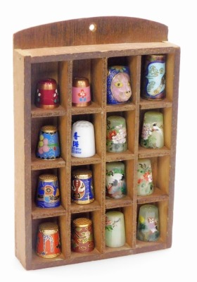 A group of Chinese cloisonné enamel, painted, jade and other thimbles, contained in a wooden wall mounted case. (16)