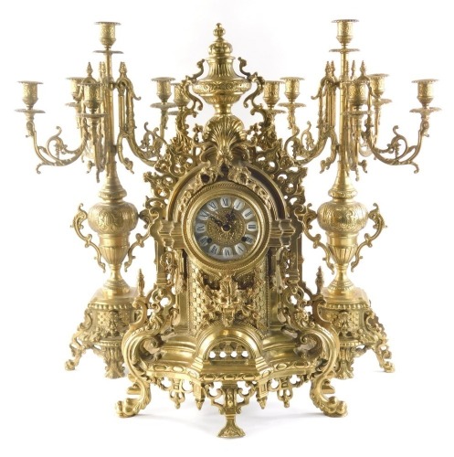 A highly elaborate 20thC French clock garniture, the clock surmounted by an urn with various scrolls, rococo flower heads, etc., with a 9cm diameter Roman numeric dial, on heavy cast metal case on serpent feet, with partially signed strike on gong movemen