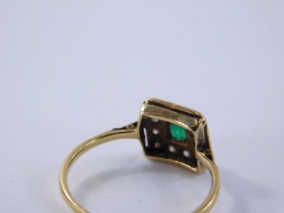 An emerald and diamond set dress ring, the square set panel with rectangular cut emerald in rub over setting surrounded by tiny diamonds, on a yellow metal band unmarked, ring size J, 1.4g all in. - 2