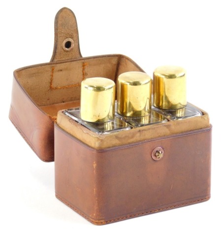 A 20thC three bottle cased cologne set, in brown leather case, each removable bottle with gilt coloured lid, of square shouldered form, the case 10cm wide.