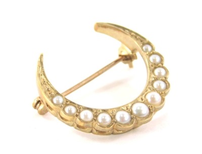 A crescent moon brooch, set with eleven seed pearls, ranging from 2mm to 3mm, in a yellow metal setting with single pin back and revolver clasp, yellow metal marked 9ct, 2.5cm wide, 3.1g all in.