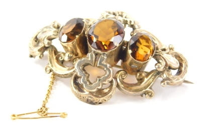 A citrine bar brooch, quatrefoil shaped with three oval cut citrines, in a yellow metal setting, unmarked with safety chain and steel pin back, tests as 9ct gold, 6cm wide, 18.7g all in.