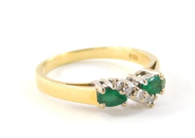 An 18ct gold emerald and diamond dress ring, set with two pear cut emeralds, each stone approximately 0.20cts, in a white four claw setting, with cross over central band set with three tiny diamonds, totalling approximately 0.05cts, on a yellow metal band