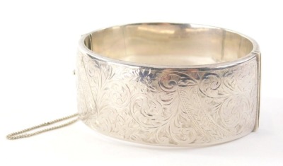 A 20thC silver hinged bangle, with heart engraved design of scrolls and vines, Birmingham 1949, engraved MBT, with safety chain, 6cm diameter, 47.2g all in.