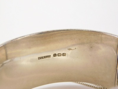 A 20thC silver hinged bangle, with heart engraved design of scrolls and vines, Birmingham 1949, engraved MBT, with safety chain, 6cm diameter, 47.2g all in. - 2