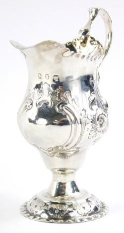 A George III silver cream jug, the helmet shaped body with ear handle repousse decorated with scrolls and flowers, on an inverted base and domed foot, London 1774, 13cm high, 2oz.