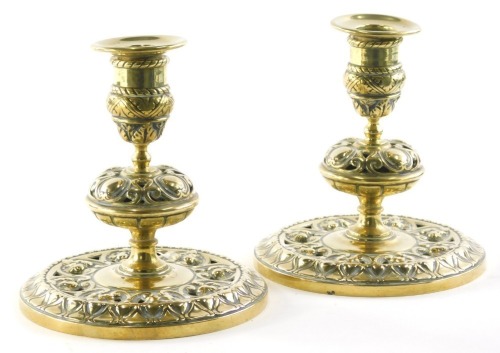 A pair of 19thC brass squat candlesticks, with urn dish holders, bellied circular bodies, inverted stems and pierced circular feet, profusely decorated with lotus flowers, foliate scrolls, panel decoration and other flower heads, 18cm high. (2)