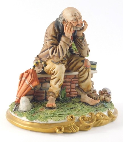 A 20thC Capodimonte figure, of a tramp on a stone wall, side book, shoes and umbrella, gilt scroll base, marked beneath, 21cm high.