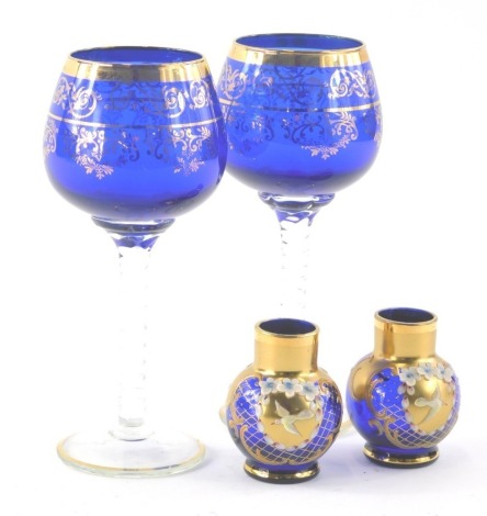 A pair of Bohemian blue glass wine goblets, with turned stems and gilt highlights, 18cm high and a further pair of blue glass vases highlighted with birds, flowers and scrolls.