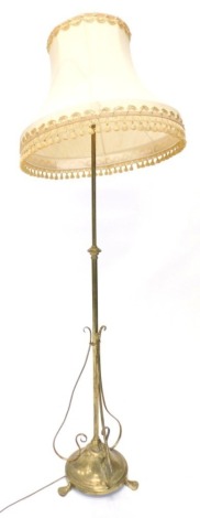 An early 20thC brass Art Nouveau floor lamp, with adjustable column the base with three scroll brackets on tapering feet with a shade, 185cm high.